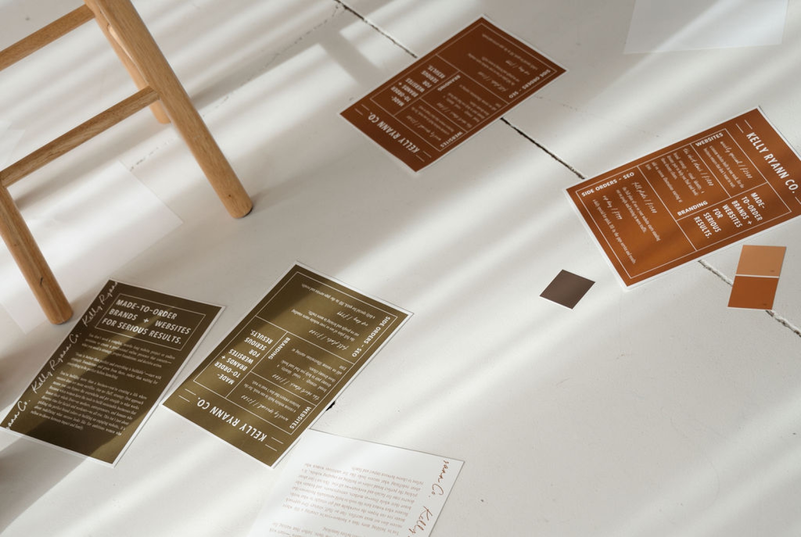 Tan and green papers with a web designers package offerings scattered on a white floor around a stool
