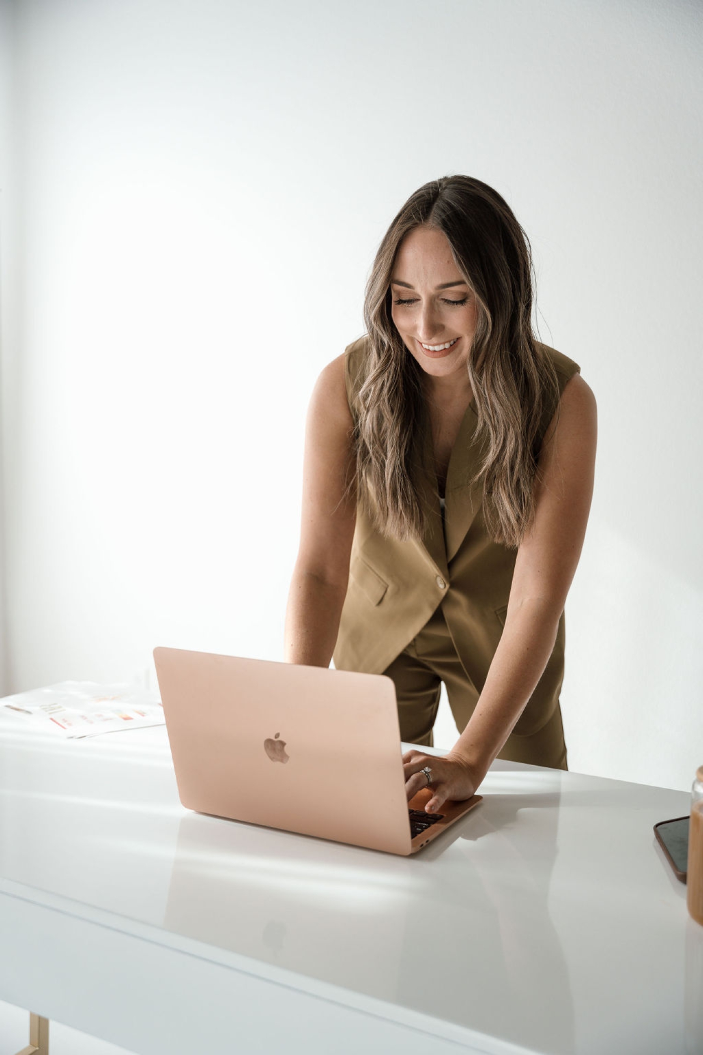 A woman in a suit leans over a laptop, typing